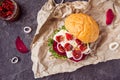 Vegitarian burger with beet slices, microgreen sprouts, tofu cheese, dried tomatoes and onion on kraft package paper on dark stone