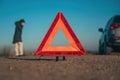 Vehicle breakdown, red warning triangle on the road with a broken down car and woman making a phone call to road service Royalty Free Stock Photo