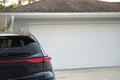 Vehicle parked in front of wide garage double door on paved driveway of typical contemporary american home