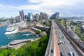 Vehicles cruise along Cahill Highway that projects straight ahead into distance and city skyline with Sydney Harbor of left,