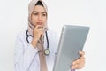 veiled doctor wearing white suit uniform confused with hand holding chin when looking at tablet screen