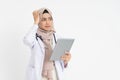 veiled female doctor wearing white suit uniform confused while looking at pad screen with hand scratching head