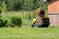 A senior man with a lawn mower mows the grass in the yard of country house