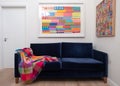 Velvet blue sofa with colourful wool blanket throw, in minimalist setting with white walls and colourful artwork.