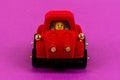 Velvet red toy car with driver on a background of light cherry color close up