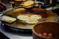 Vendor hand frying round roti dough in hot pan