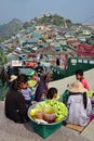 Vendors selling raw cut mango plus dark sauce and plum powder with large community over a small hill behind