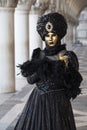 Person wearing a Venice mask and black and gold costume under Arcade of Doge's Palace at the Venice Carnival in Venice Italy