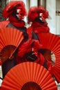 Three Venice masks dressed in red and black costumes holding red fans at the Venice Carnival in Venice Italy