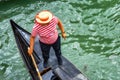 Venetian gondolier punting gondola through green canal waters of Venice