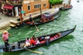 Venetian gondolier punting gondola through green canal waters of Venice