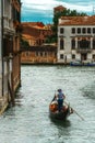 Venetian gondolier punting gondola through green canal waters of Venice
