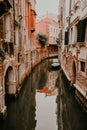 Venetian narrow water channels with green water and tall brown old buildings all around.