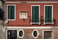 Venetian red facade of old house with religious scene, green windows and typical oval windows. Venice, Italy Royalty Free Stock Photo