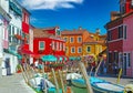 View over water canal with boats on brightly garish colored houses and tre ponti bridge, blue sky, fluffy cloud