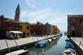 Venice canal with boats and colorful houses and church on Burano island,