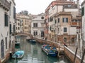 Venice canal scene depicting small boats in a quiet residential part of Venice in winter on a cool grey day with a few people on Royalty Free Stock Photo