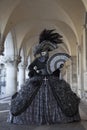 Venice mask dressed in a silver and black costume and mask under arches of Doge's Palace at Venice Carnival in February