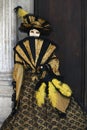 Venice Carnival figure wearing colourful gold and black costume and venetian mask with a fan Venice Italy Royalty Free Stock Photo