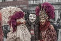 Venice Carnival. A man in Guy Fawkes mask is posing with a costumed masked woman with a parasol and a costumed masked man