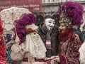 Venice Carnival. A man in Guy Fawkes mask is posing with a costumed masked woman with a parasol and a costumed masked man Royalty Free Stock Photo