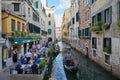 Restaurant with sidewalk tables people and gondola passing in the canal in Venice, Italy