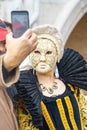 VENICE, ITALY - 23.02.2019: Beautiful mask and man take a photo on mobile phone at St. Mark square during the carnival of Venice