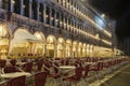 Venice, Italy empty Saint Mark square with arcades at night. Illuminated view of closed stores with empty red chairs stacked Royalty Free Stock Photo