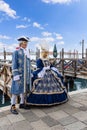 A couple of participants in elegant baroque costumes pose on the embankment at the Venice Carnival