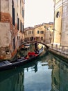Venice, Italy - February 2019: Gondolier in a venetian canal. Two little girls looking at him from bridge
