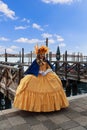 A participant in the Venice Carnival in an original yellow costume and mask poses on the embankment