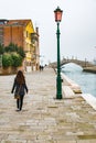 Snapshot of a woman crossing walking alone by the river with the people and the houses