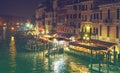 VENICE, ITALY - 02.23.2019: Gondolas moored on Grand Canal in Venice. Tourists in cozy restaurants outdoors. Grand Canal at night, Royalty Free Stock Photo