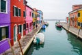Venice, Italy - January 2020: Colorful houses in Burano Island along quaint canal with boats docked at riverside