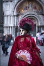 Masked woman in red dress with purple featheres on black hat and hand fan at Venetian carnaval Royalty Free Stock Photo