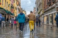 VENICE, ITALY - May 23, 2016: Male couple in colorful cloths from back walking through Venice streets after storm with umbrellas