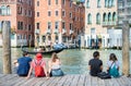Tourists sitting on a wooden boat pier and enjoying the idyllic scene on Grand Canal in Venice