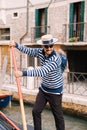 Venice, Italy - 04 october 2019: A smiling happy gondolier controls a gondola with tourists using a paddle. The classic