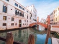 Venice, Italy - 17.10.2023: Red brick bridge reflects in blue color water and light color buildings. Warm sunny day