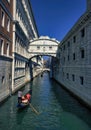 Venice, Italy: A man rowing gondola boat with passengers on a green water canal through famous bridge of sigh Royalty Free Stock Photo