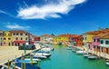 Picturesque view on water canal with boats, bridge, bright colorful houses against clear blue sky, fluffy cloud