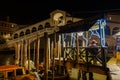 Venice, Italy night view of Ponte di Rialto, Rialto pedestrian Bridge with a gondolier next to wooden wharf pilings. Royalty Free Stock Photo