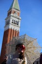 Venice, VE, Italy - February 13, 2024: girl with mask and lipstick and umbrella and bell tower during Carnival Royalty Free Stock Photo