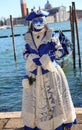 Venice, VE, Italy - February 13, 2024: masked woman with luxurious white and blue dress on the seashore Royalty Free Stock Photo