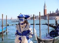 Venice, VE, Italy - February 13, 2024: masquerade woman with luxurious dress of white and blue color on the seashore and a gondola