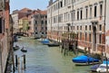 Venice water canal, typical Venetian architecture, boats parked by the canal, blue and red posts on the Venice canal, greenish wat Royalty Free Stock Photo