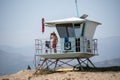 A male lifeguard at Ventura Harbor watches from inside a lifeguard tower at a breakwater