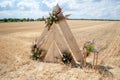 Venue for a wedding ceremony in rustic style in a rural place. Triangular arch decorated with flowers in a golden, mown field. Royalty Free Stock Photo