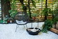 Veranda of house with black Acapulco armchairs, coffee table and green plants in pots. Metal black fireplace bowl in garden on bac