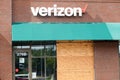 A Verizon store in an outdoor strip mall with a plywood panel covering a broken glass front window